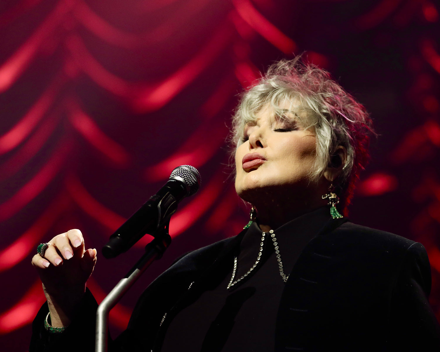 Ann Wilson singing in front of a microphone with a red velvet backdrop